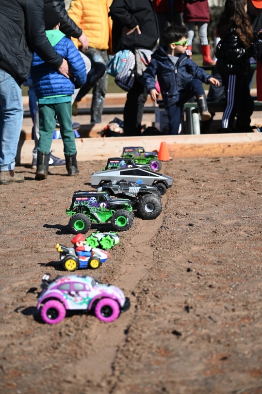 Radio-controlled toy cars line up at the starting line on the dirt track of the baseball diamond.